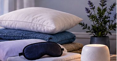 Stacked pillows and blankets with a sleep mask and a white-noise machine
